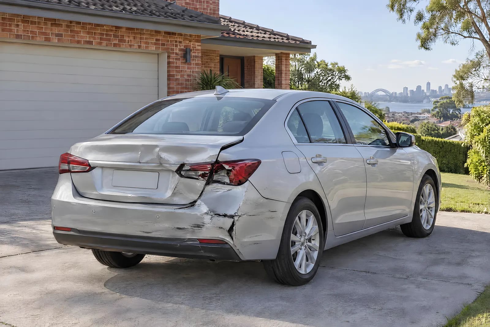 A silver sedan with a crumpled boot lid, a pushed-in rear bumper and a broken tail light before repair