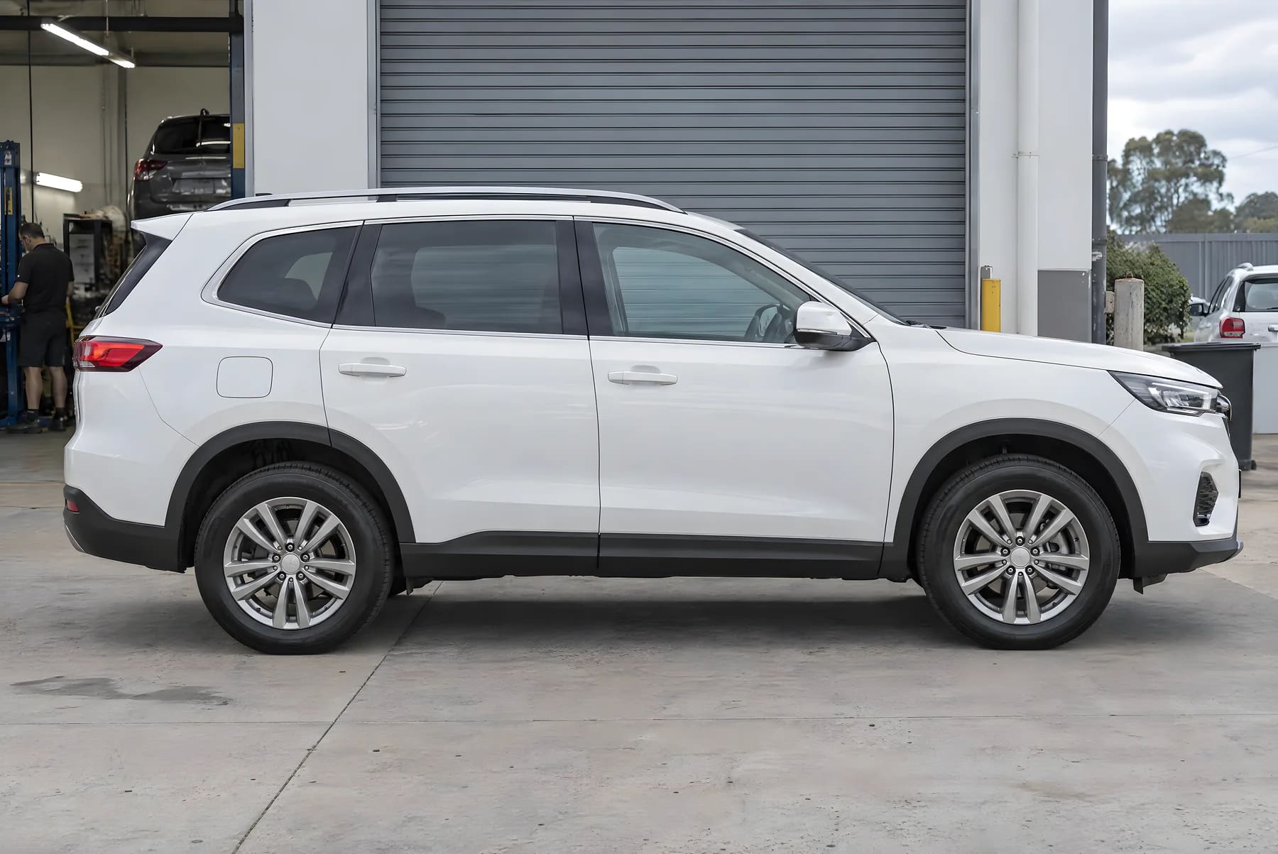 The same white family SUV after repair, with flat panels and even paint, outside a smash-repair workshop