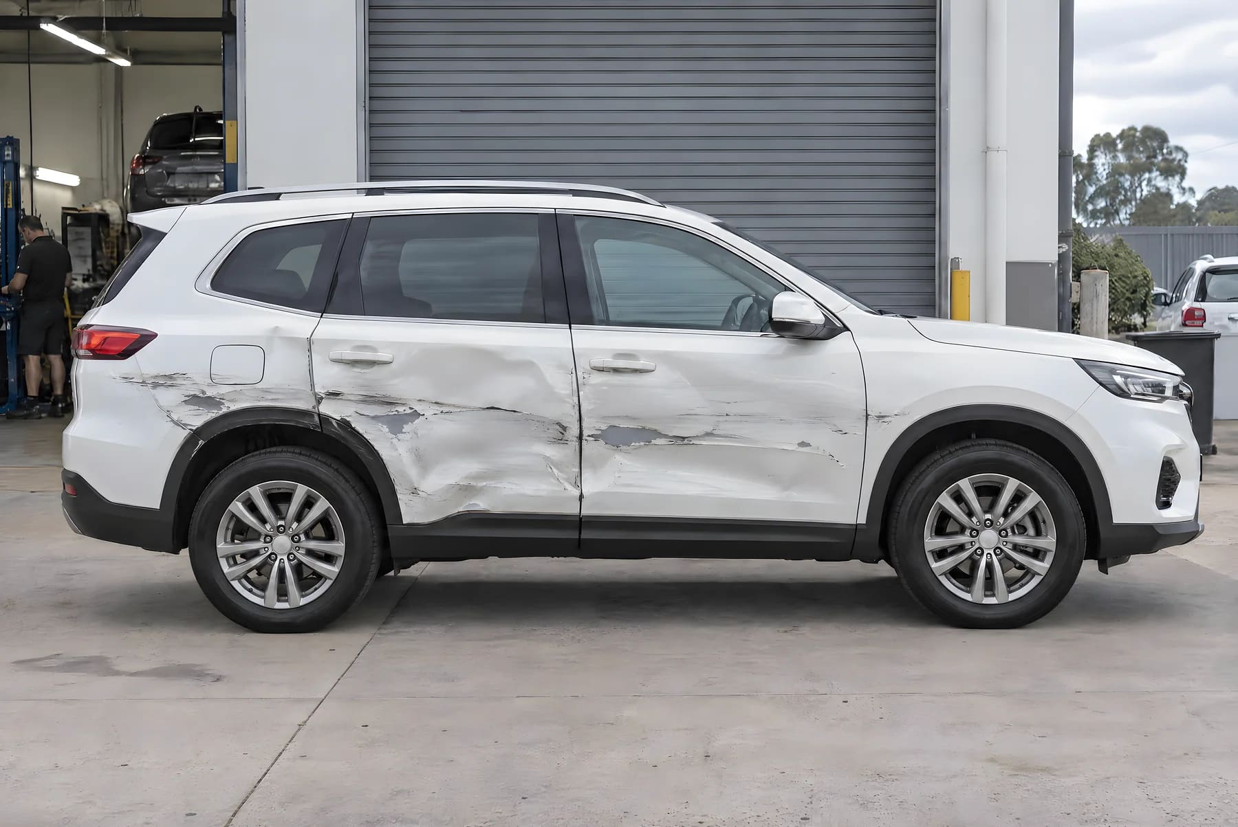 A white family SUV with dented door panels and deep paint scrapes running along both doors and the rear quarter panel before repair