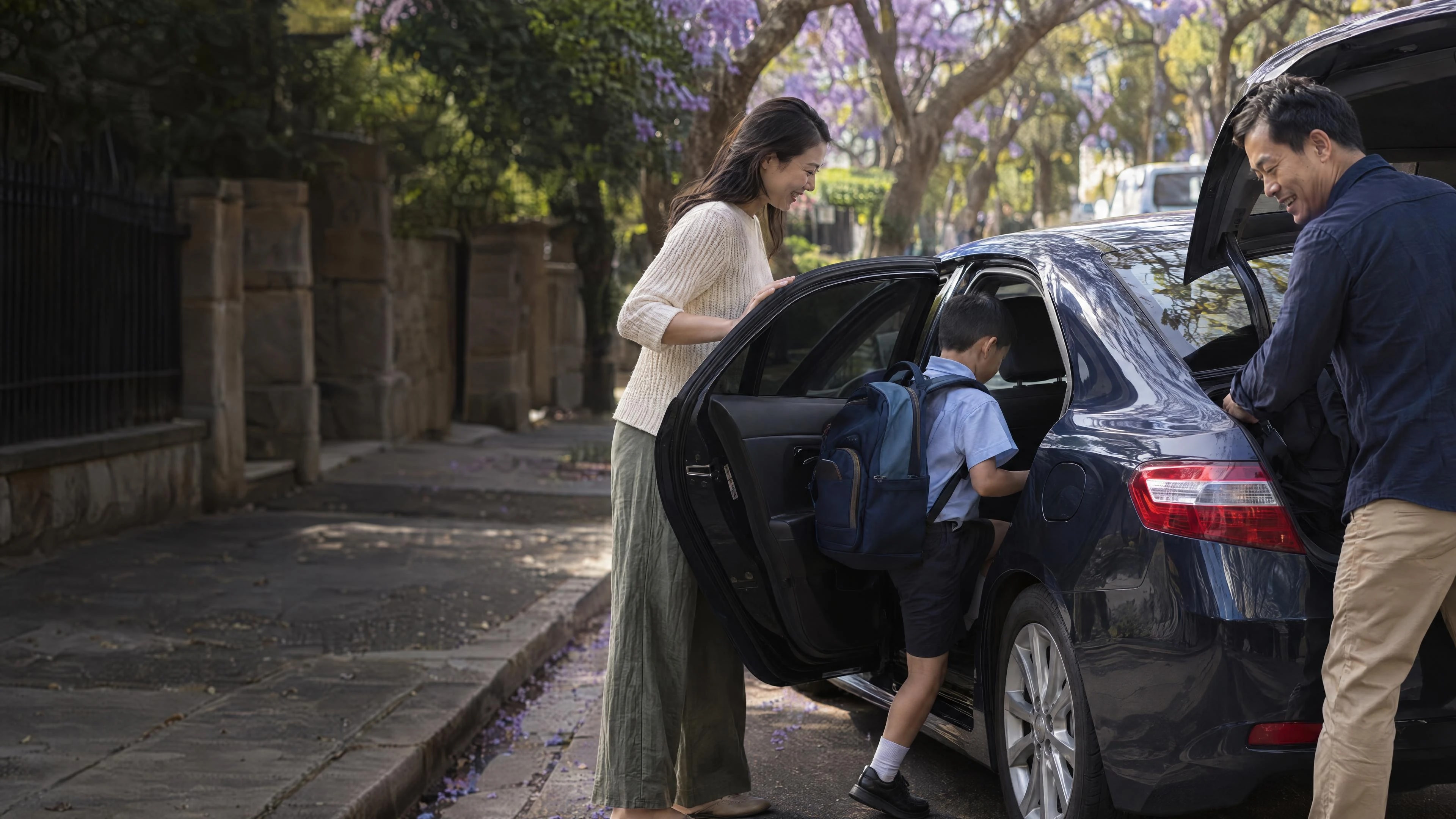 A Chinese-Australian family gets into a dark blue replacement sedan on a leafy Sydney street in late-afternoon sun; the mother holds the rear door as her son climbs in, while the father smiles at the open boot
